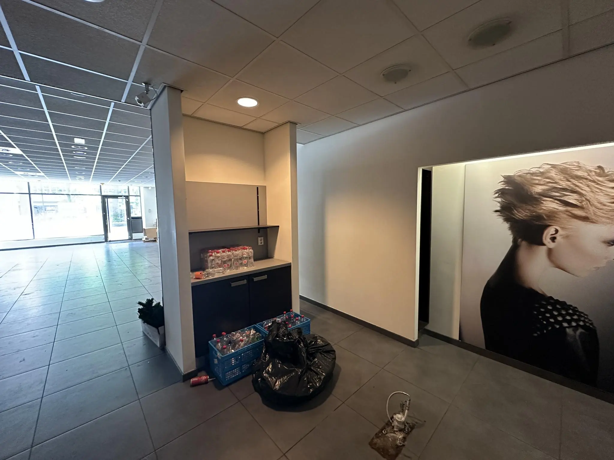 Leegstaand winkelpand aan de Coolsingel met lege flessenkratten en een grote poster van een model met korte kapsel.