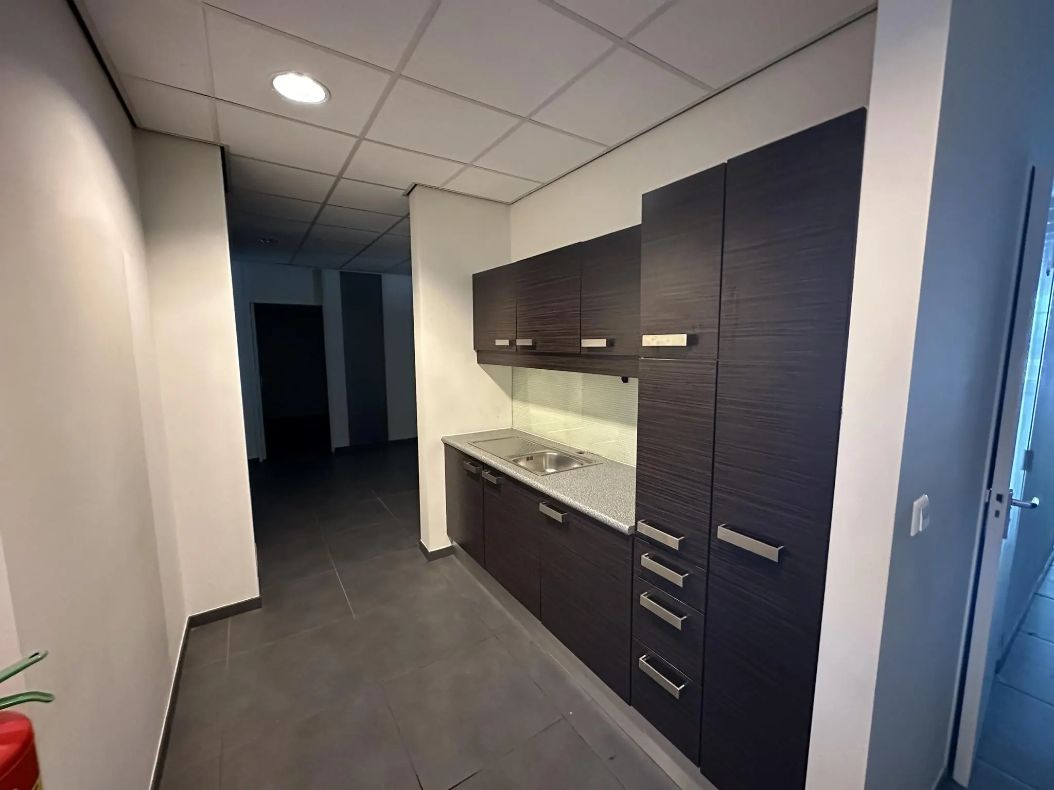 Keukenblok met donkere kastjes en grijs werkblad in een gang van een kantoorpand aan de Coolsingel.