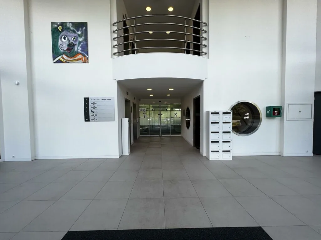 Ingang van een modern kantoorgebouw met brievenbussen, een schilderij aan de muur en een overzichtsbord van bedrijven aan de Nevelgaarde.