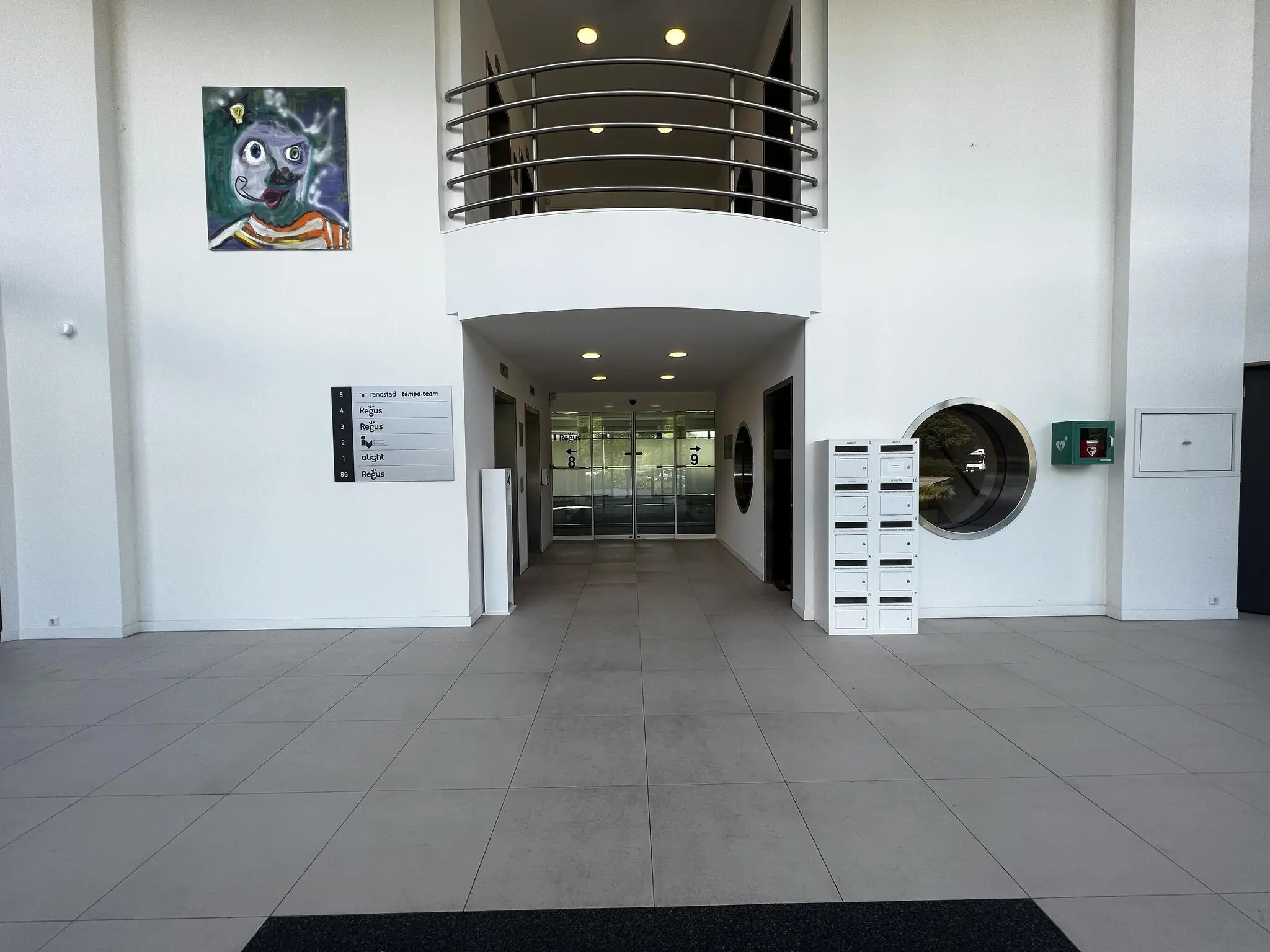 Ingang van een modern kantoorgebouw met brievenbussen, een schilderij aan de muur en een overzichtsbord van bedrijven aan de Nevelgaarde.