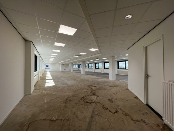 Lege kantoorruimte in Nevelgaarde met systeemplafond, grote ramen en onafgewerkte vloer.