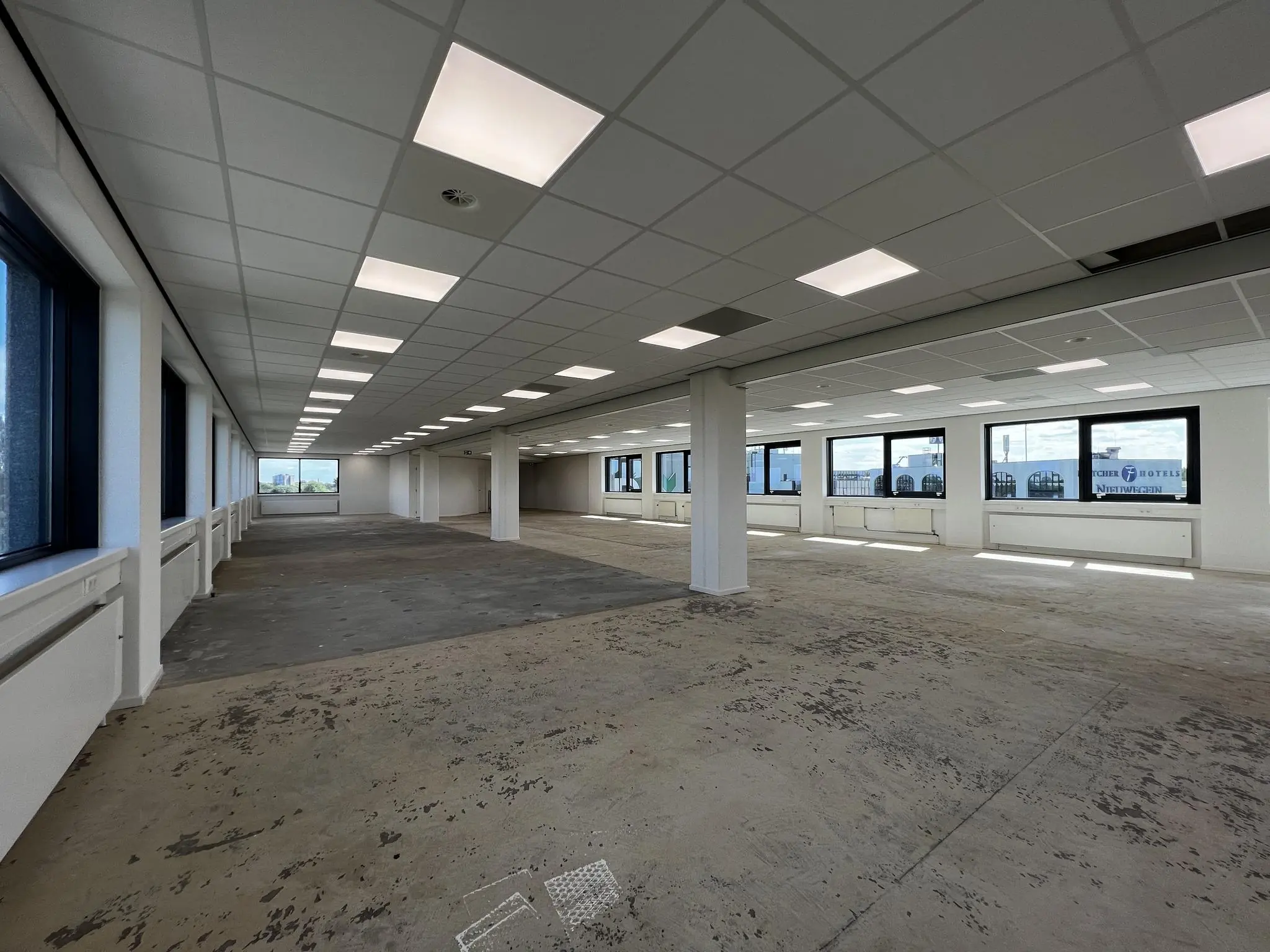 Leeg kantoorpand aan de Nevelgaarde met systeemplafond, grote raampartijen en onafgewerkte vloer.