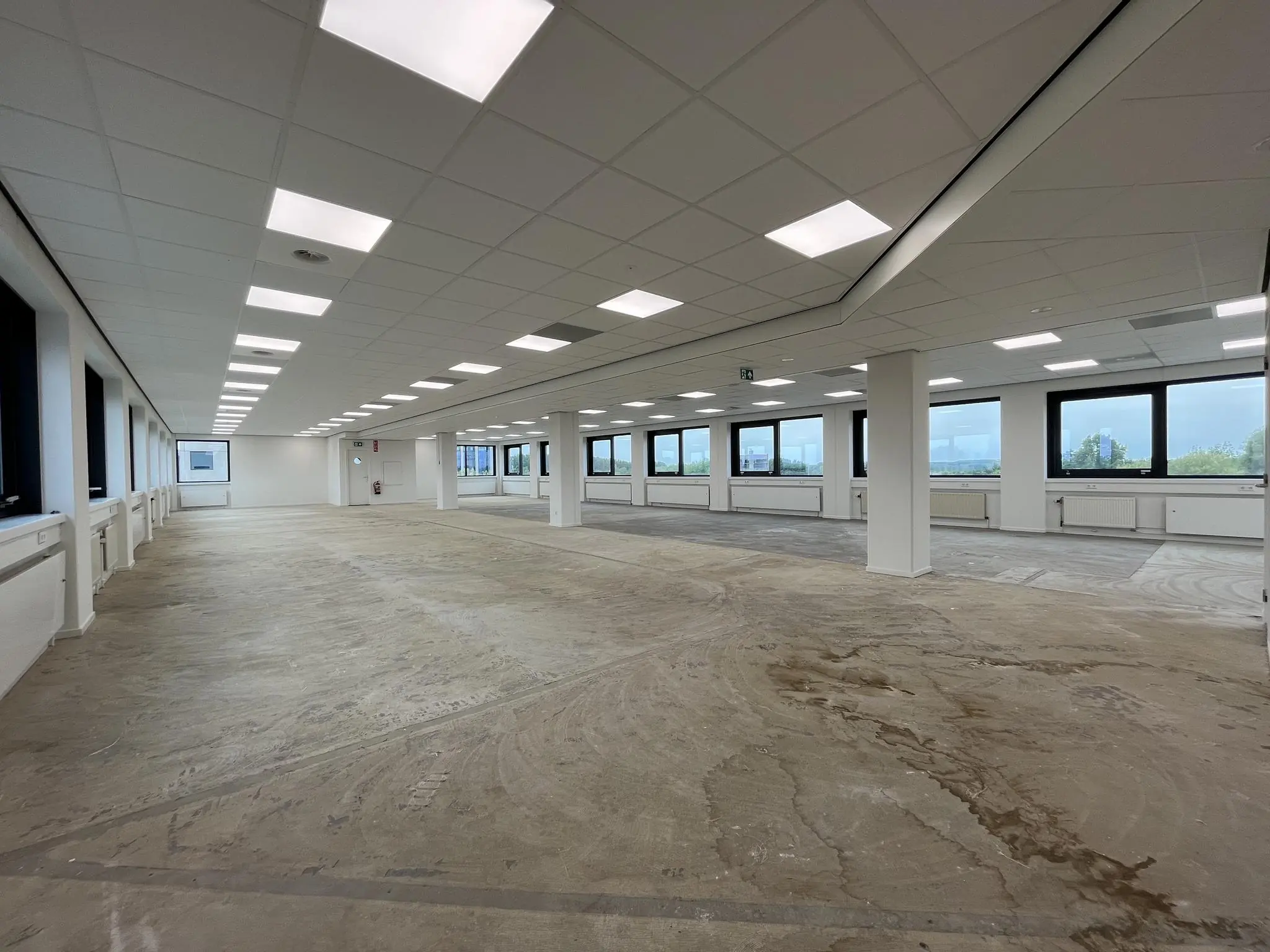 Lege kantoorruimte in Nevelgaarde met systeemplafond, kale vloer en grote ramen.