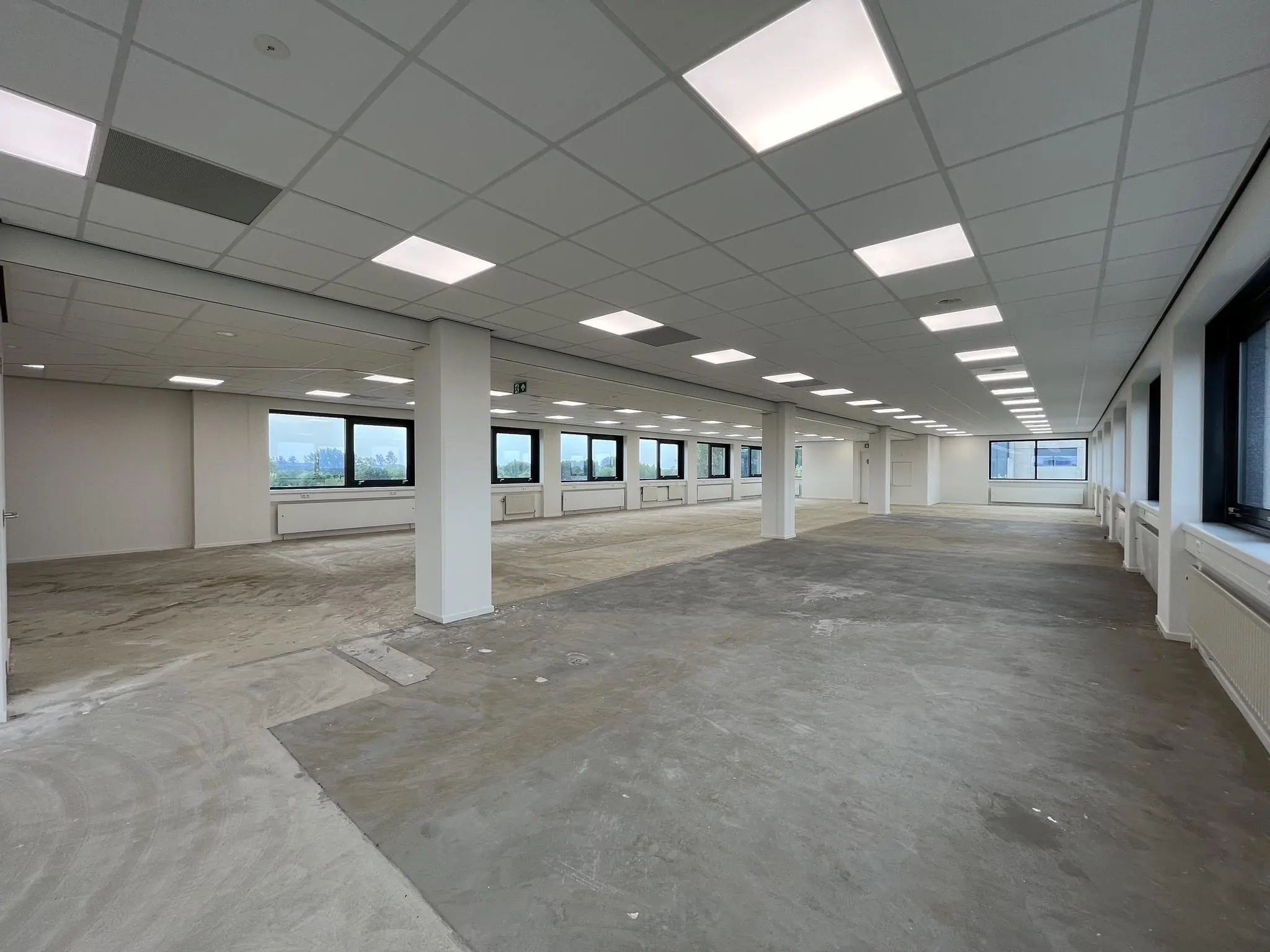 Leeg kantoorpand aan de Nevelgaarde met systeemplafond, grote ramen en onafgewerkte vloer.