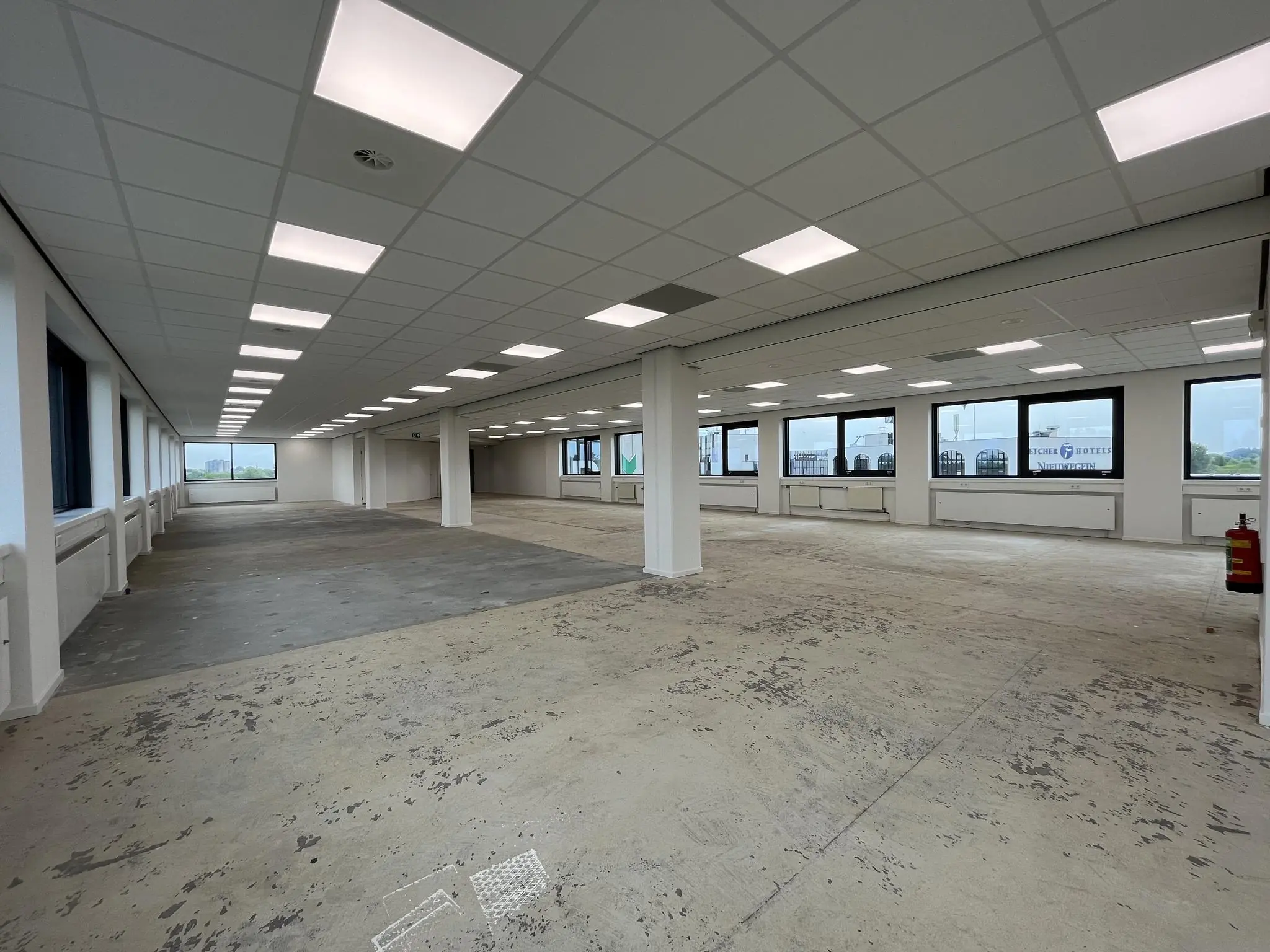 Leeg kantoorpand aan de Nevelgaarde met systeemplafond, grote ramen en onafgewerkte vloer.