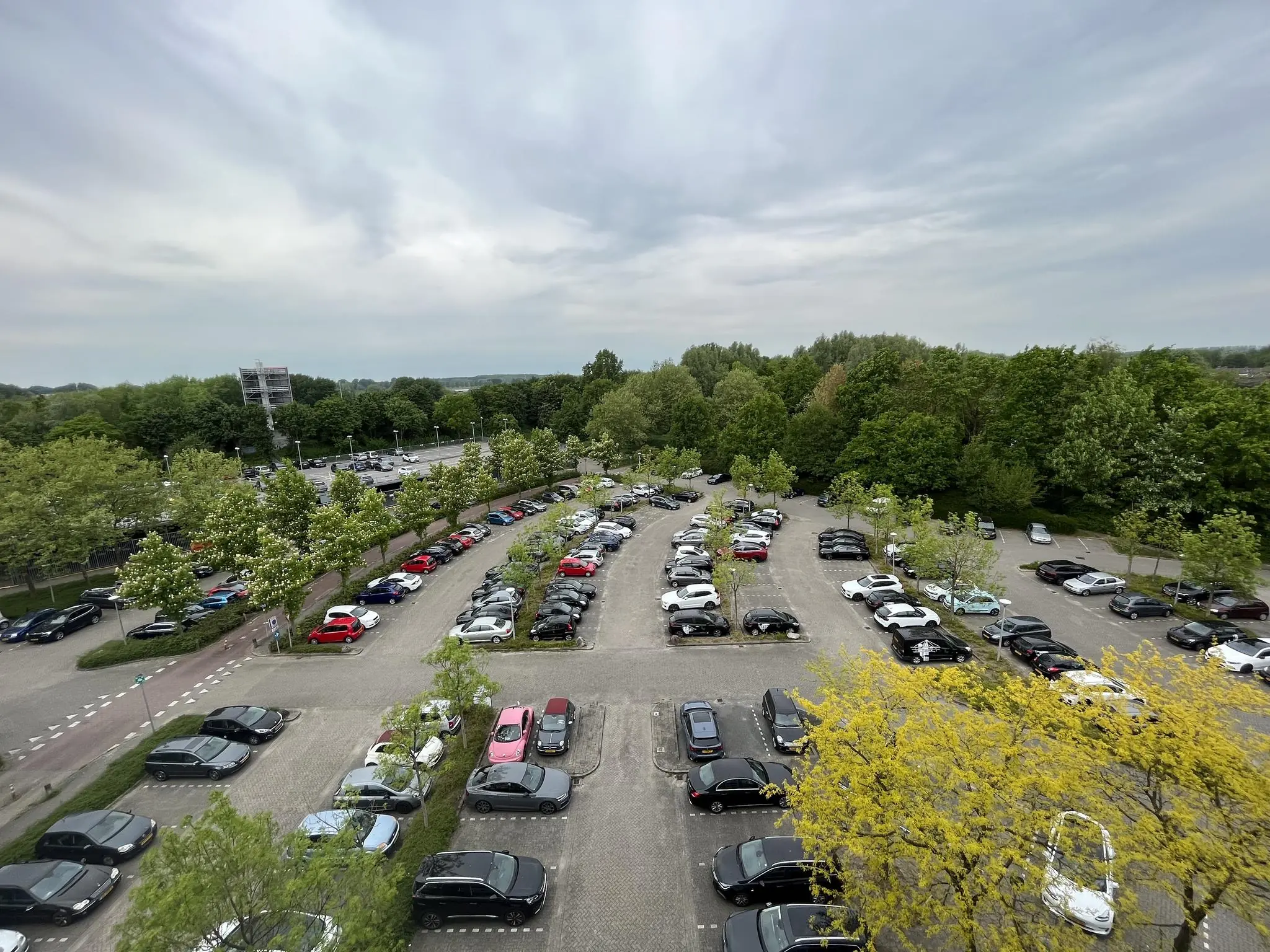 Overzicht van een grote parkeerplaats aan de Nevelgaarde, omringd door bomen en deels bezet met geparkeerde auto's.