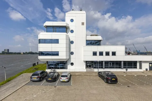 Modern wit kantoorgebouw aan de Havenstraat met parkeerplaatsen en uitzicht op het water.