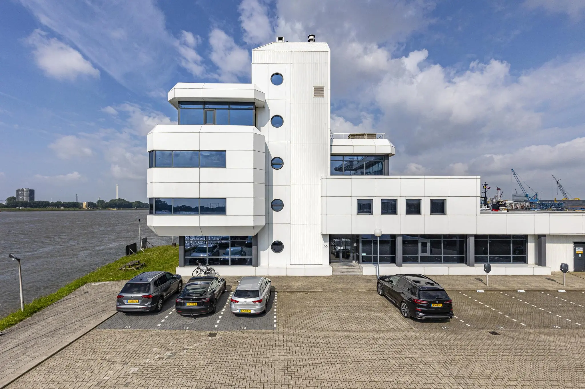 Modern wit kantoorgebouw aan de Havenstraat met parkeerplaatsen en uitzicht op het water.