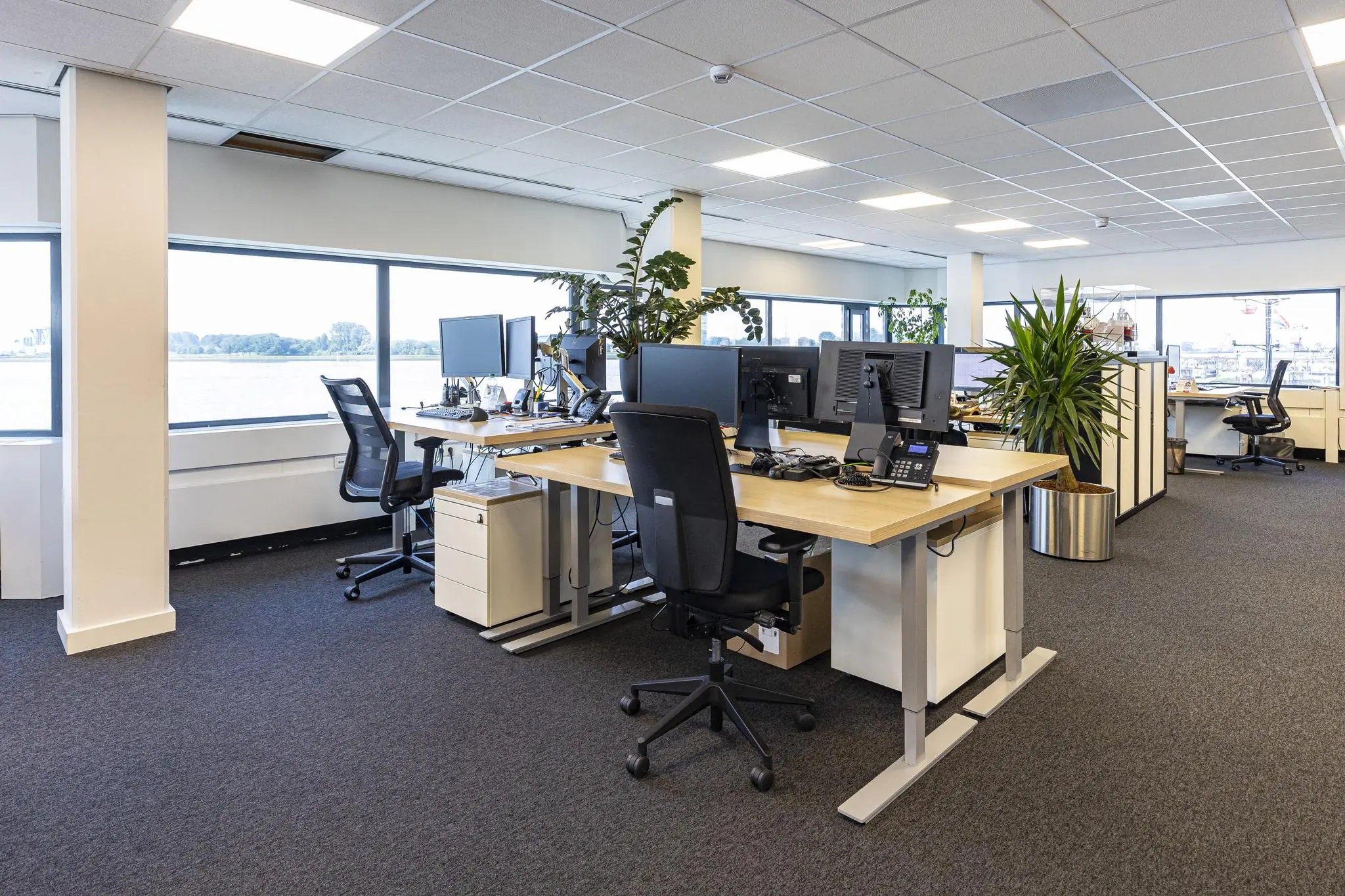Modern kantoorinterieur aan de Havenstraat met meerdere bureaus, bureaustoelen, computers en grote ramen met uitzicht op het water.