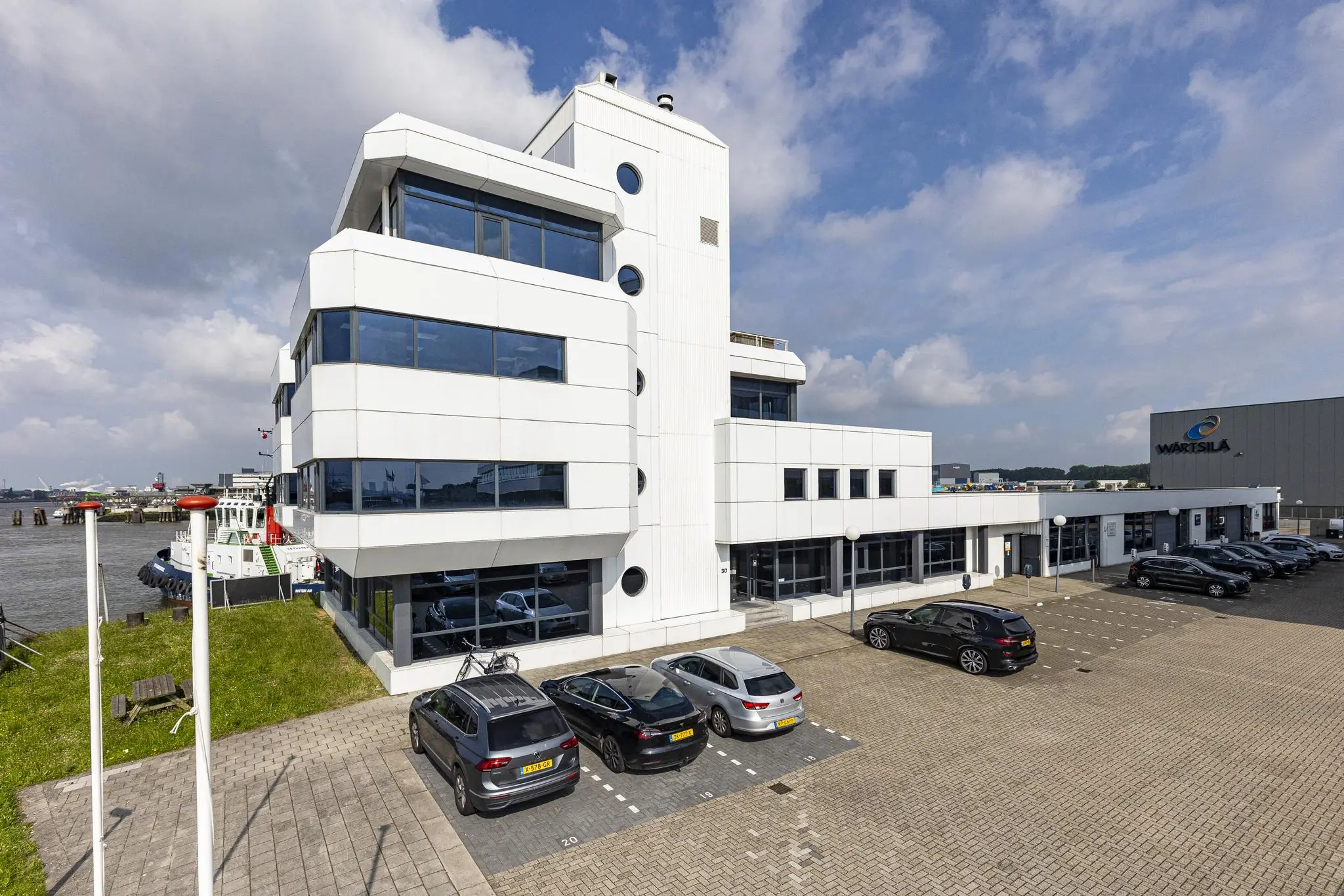 Modern kantoorgebouw aan de Havenstraat met uitzicht op het water en geparkeerde auto’s op de voorgrond.