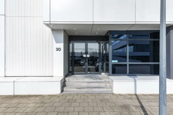 Ingang van een modern kantoorgebouw aan de Havenstraat 30 met glazen deuren en witte gevel.