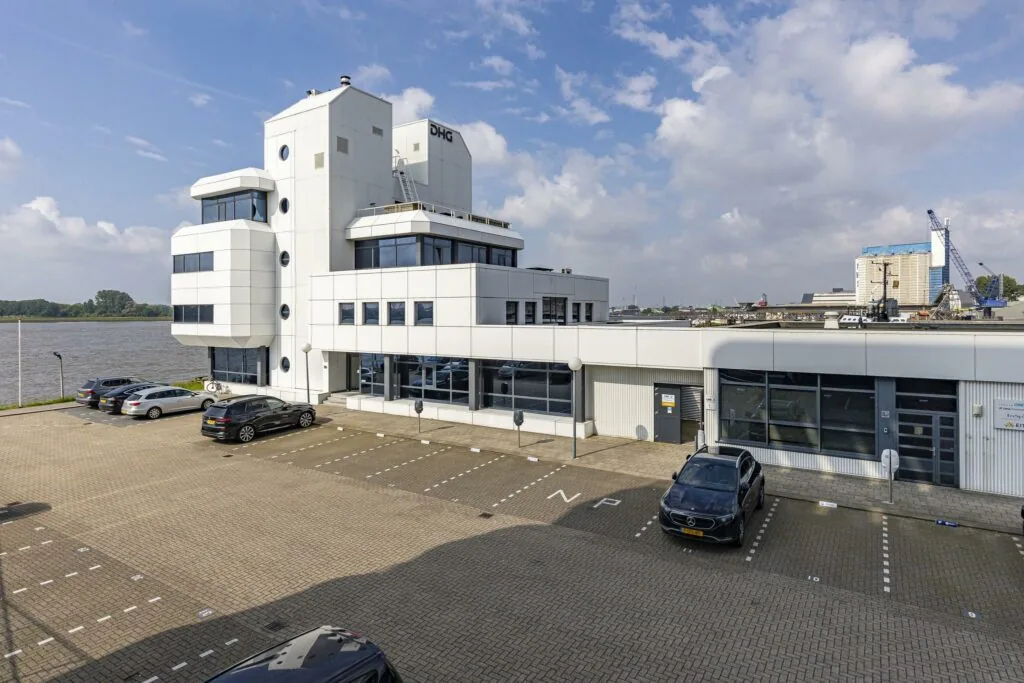 Modern kantoorgebouw van DHG aan de Havenstraat met parkeerterrein en uitzicht op het water.