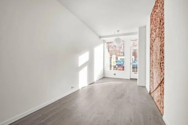 Lichte, lege kamer aan de Westerstraat met een houten vloer, grote ramen en een muur met bakstenen accent.