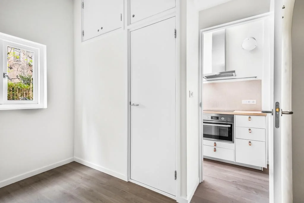 Lichte kamer met ingebouwde kasten en zicht op een moderne witte keuken aan de Westerstraat.