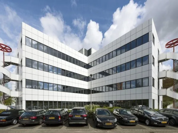 Wit kantoorgebouw aan de Entrada met spiegelende ramen en geparkeerde auto's op de voorgrond.