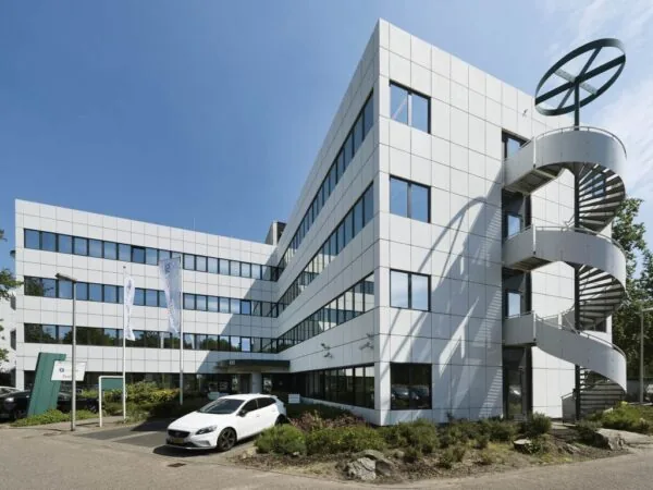 Wit kantoorgebouw met glazen ramen, buitentrap en geparkeerde auto voor de ingang van FND locatie Entrada.