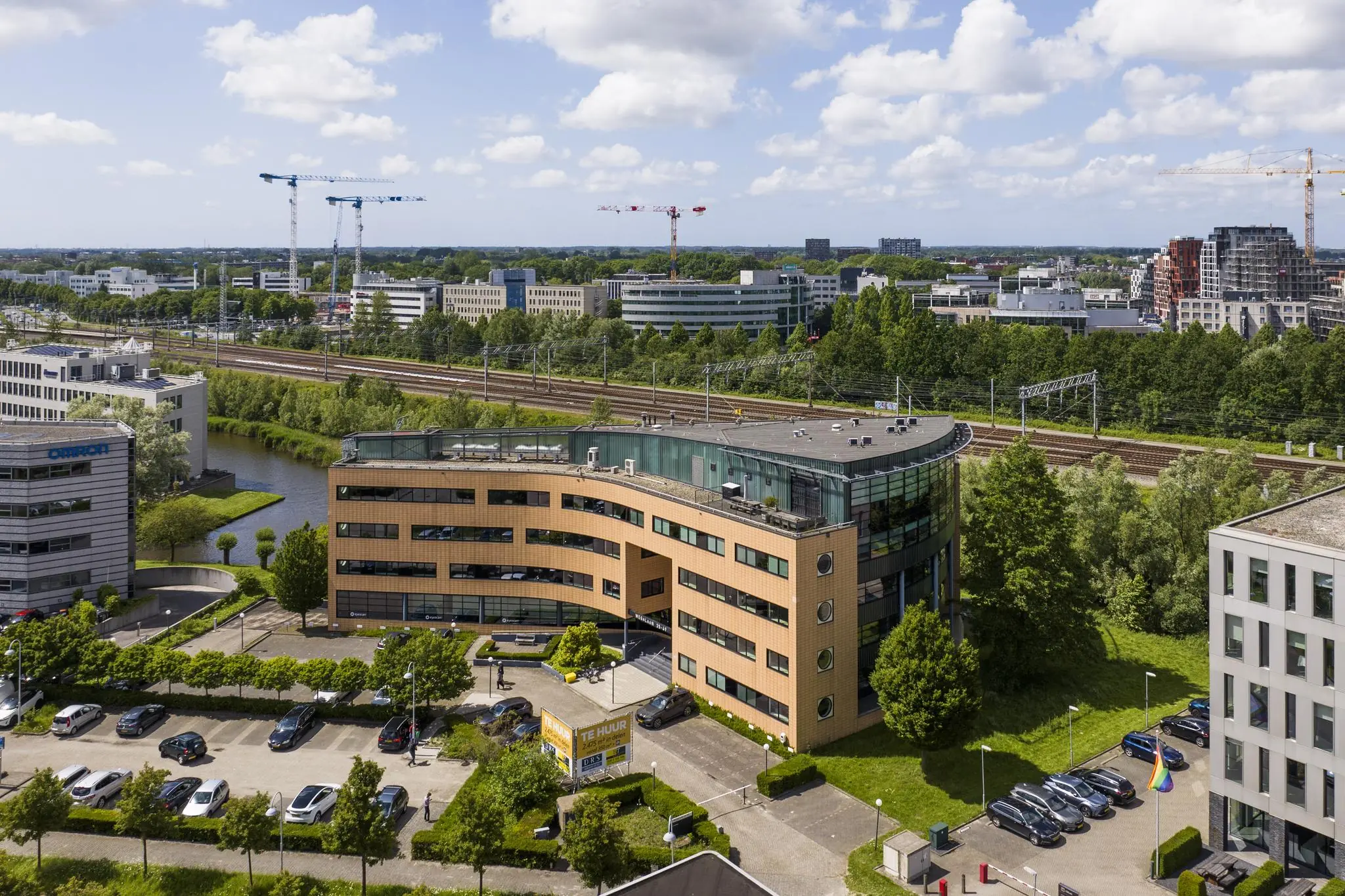Kantoorgebouw aan de Wegalaan in Hoofddorp met parkeerplaatsen op de voorgrond en spoorlijnen op de achtergrond.