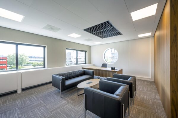 Moderne kantoorruimte aan de Wegalaan met een bureau, zithoek en grote ramen, inclusief rond raam met uitzicht.