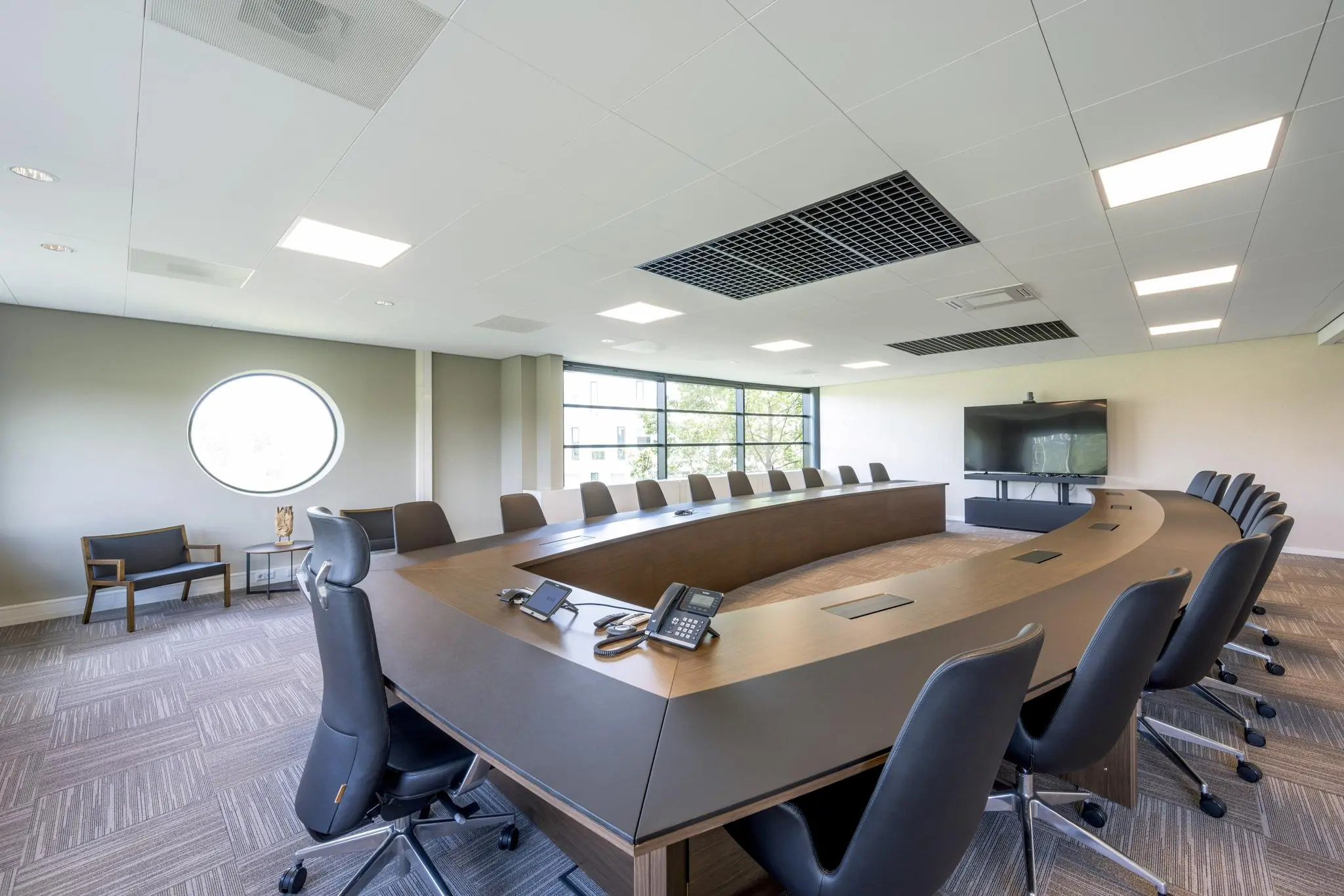 Moderne vergaderruimte aan de Wegalaan met een grote, halfronde tafel, zwarte stoelen en audiovisuele apparatuur.