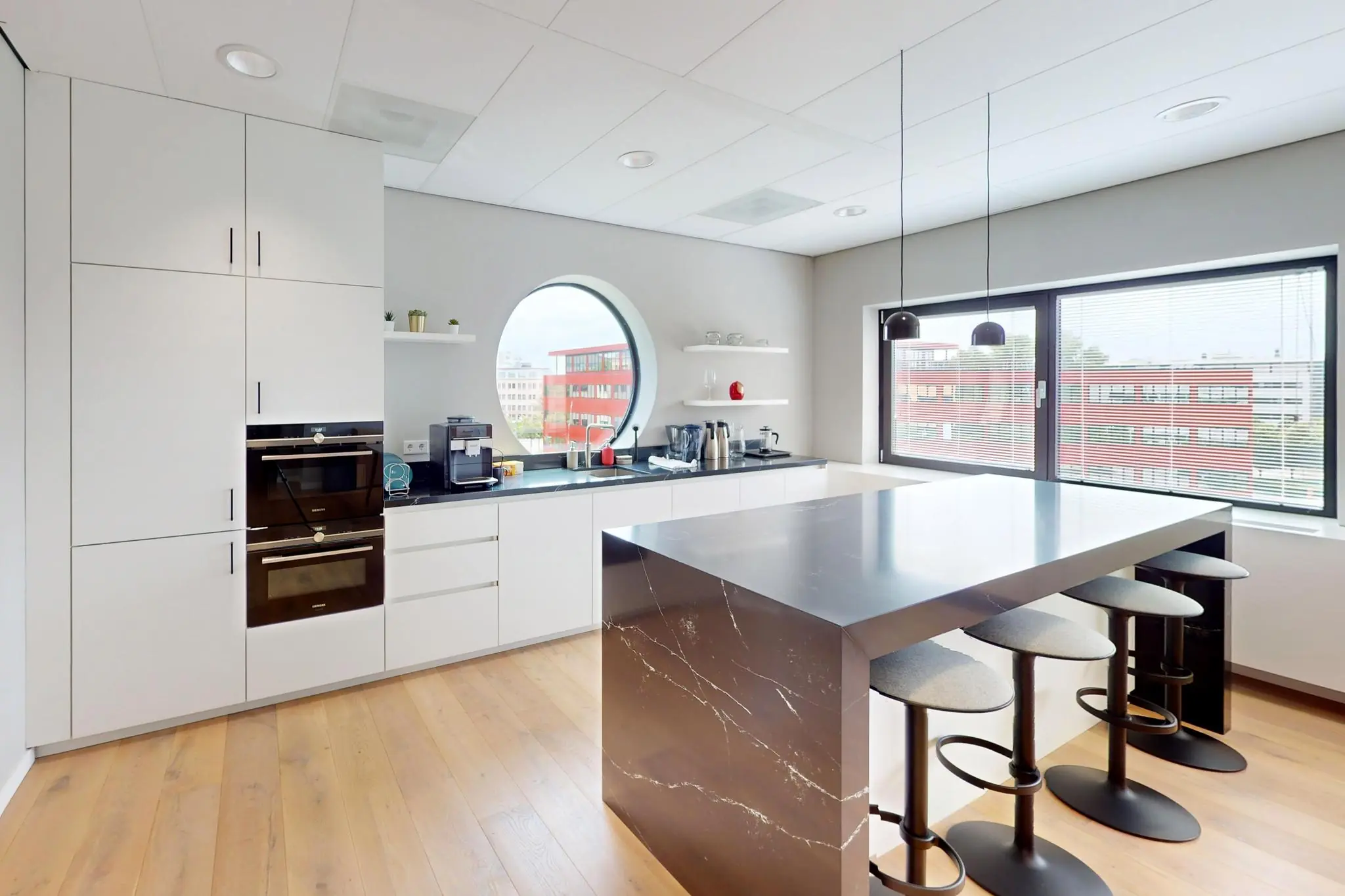 Moderne keuken met wit interieur, zwart marmeren kookeiland en uitzicht op rode kantoorgebouwen aan de Wegalaan.