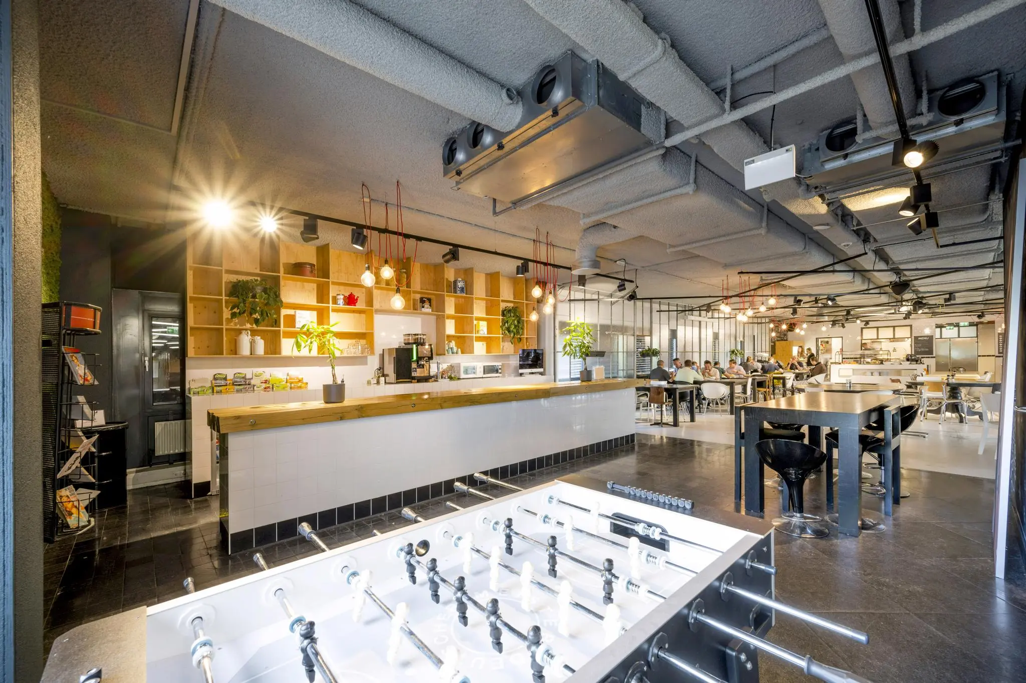 Moderne, open kantoorcafetaria in Diemermeere met een bar, zitruimte, tafelvoetbaltafel en industriële inrichting.
