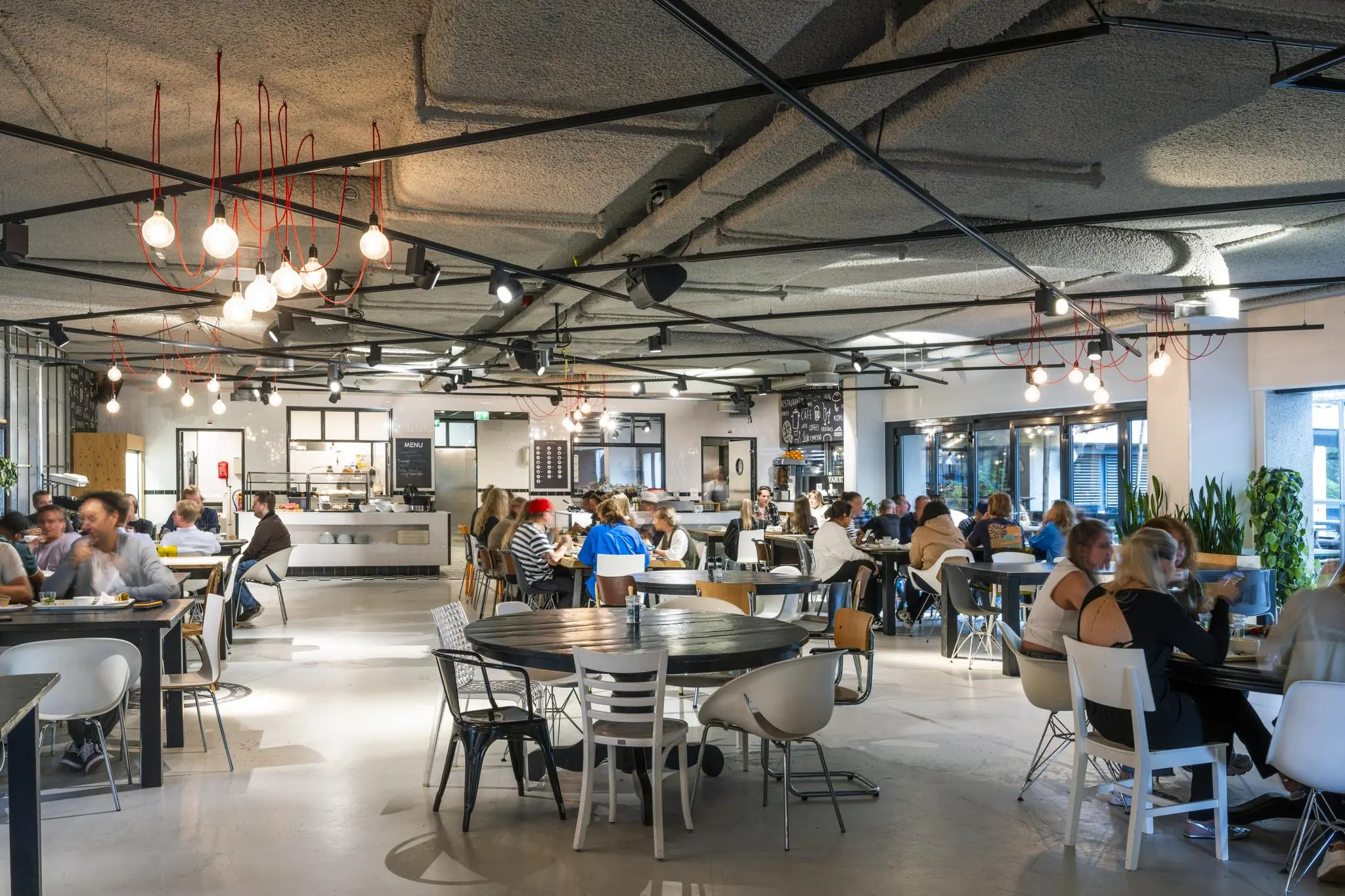 Drukke, modern ingerichte lunchruimte in Broedplaats Diemermeer met diverse mensen aan tafels.