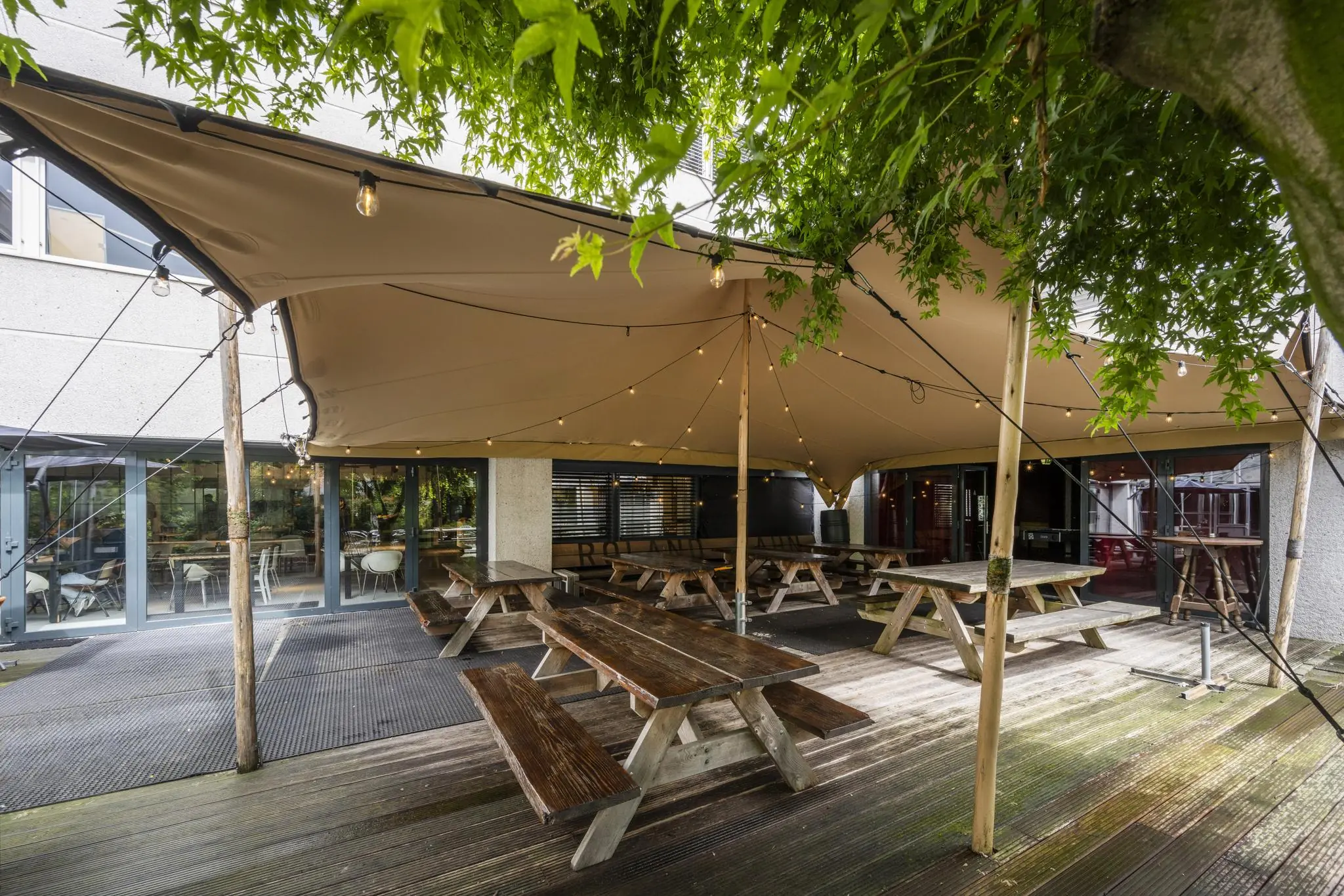 Overdekt terras met houten picknicktafels en sfeerverlichting bij Diemermeer.