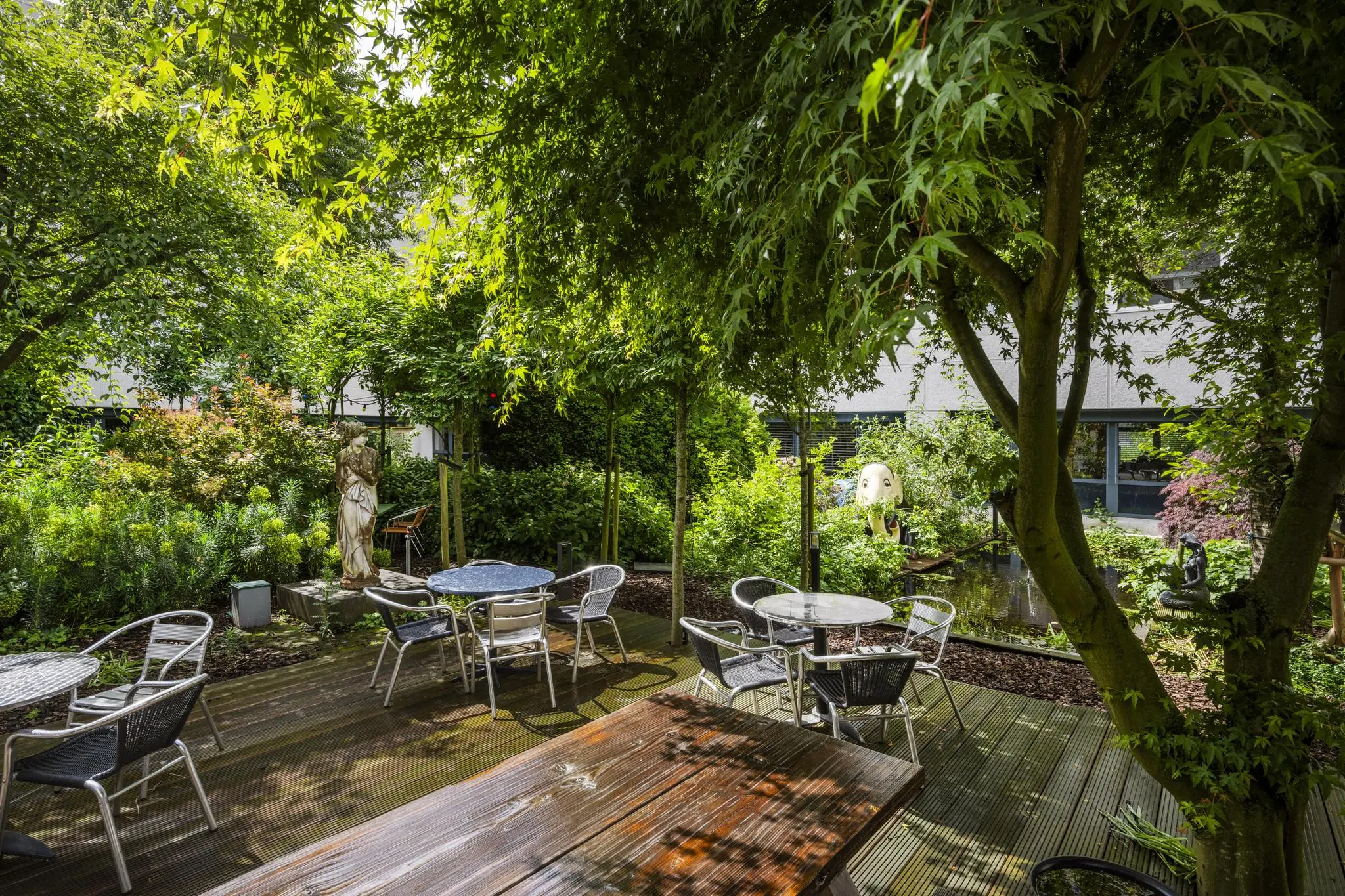 Groene binnentuin van zorgcentrum Diemermere met zitjes, beelden en een vijver.