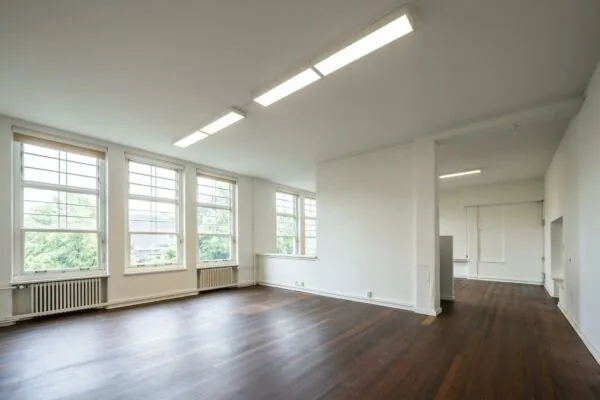 Lichte, ruime kamer met grote ramen, witte muren en een donker houten vloer aan het WG-plein.