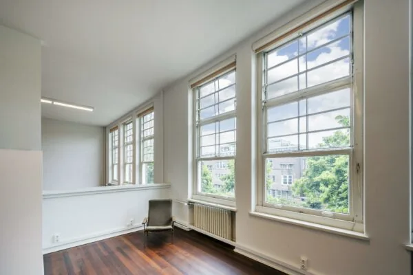 Lichte kamer met grote ramen en uitzicht op gebouwen en bomen aan het WG-plein.