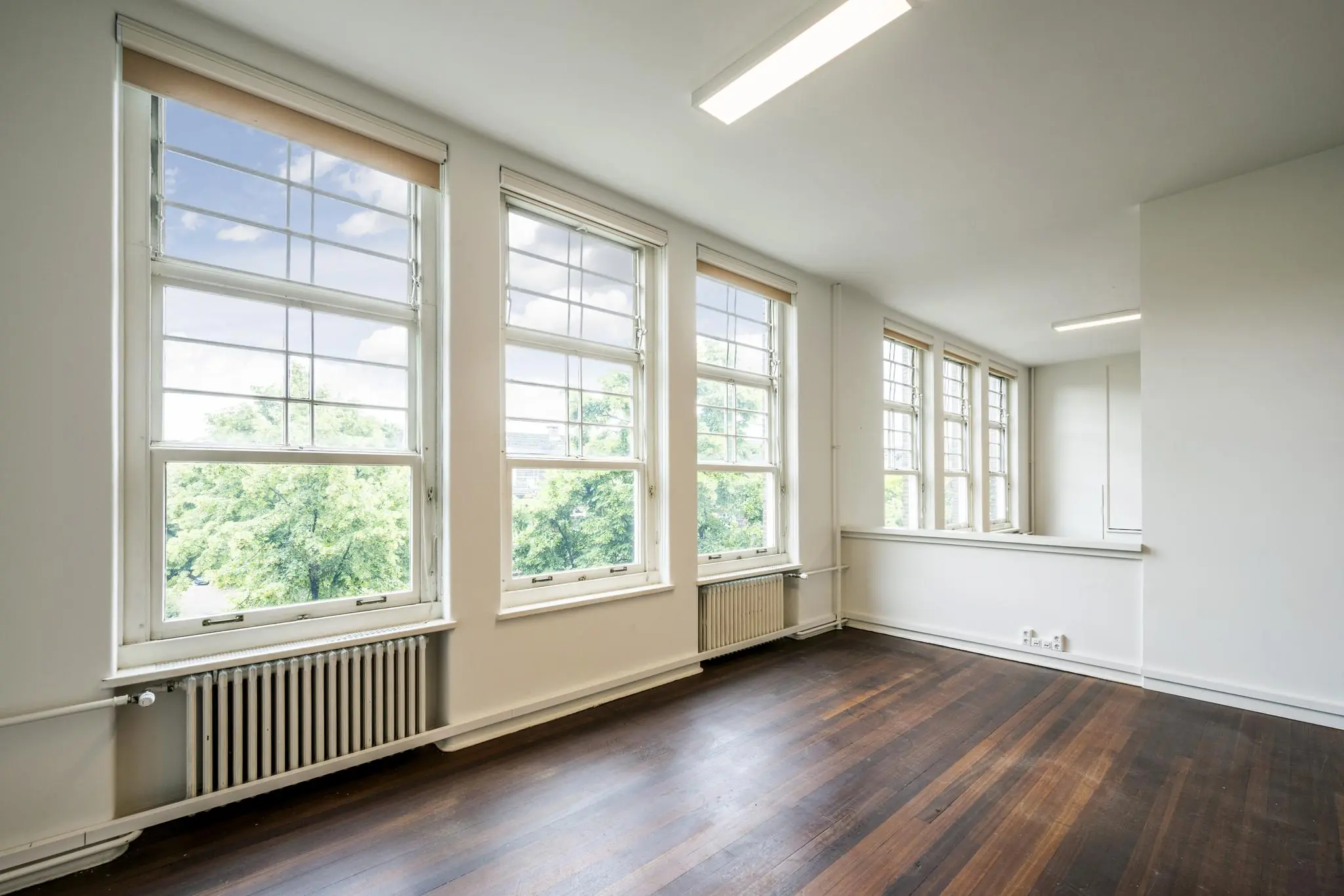 Lichte, leegstaande kamer aan het WG-plein met grote ramen en donker houten vloer.