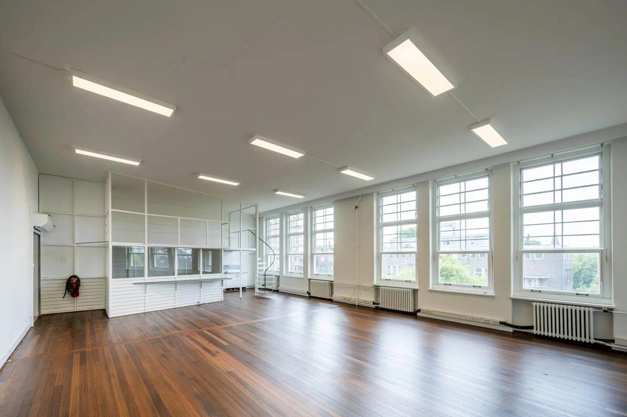 Lichte, ruime kamer met houten vloer, hoge ramen en een witte vide in het WG-plein gebouw.