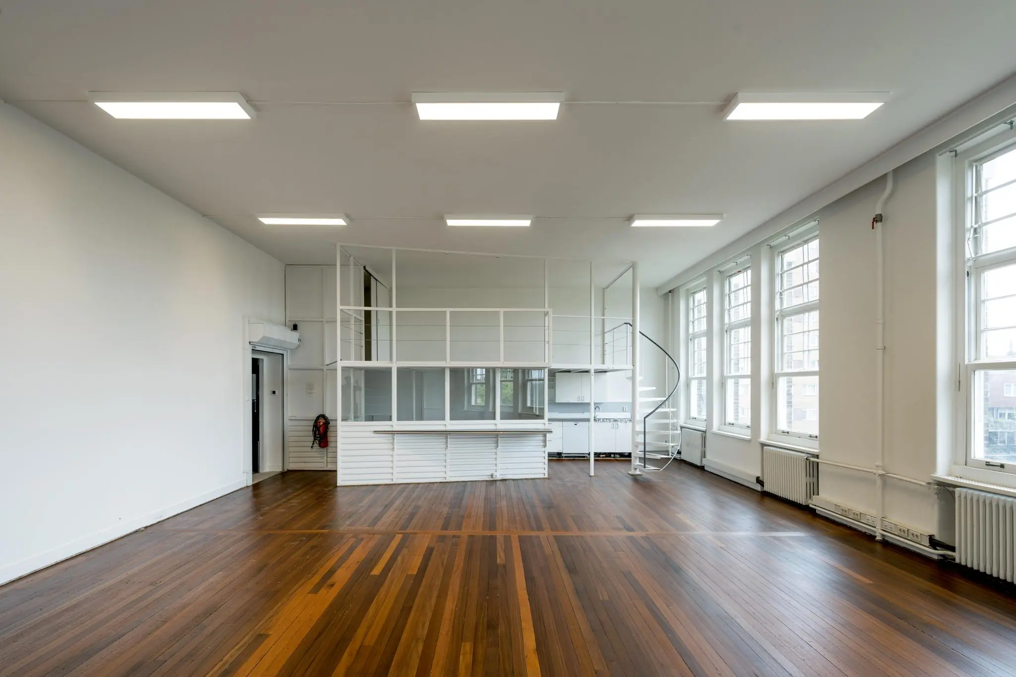 Lichte ruimte met houten vloer, grote ramen en een witte spiltrap naar een verhoogde werkplek aan het WG-plein.