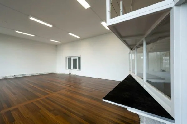 Leeg, modern binnenruimte op het WG-plein met houten vloer, witte muren en een opvallende glazen hoekconstructie.