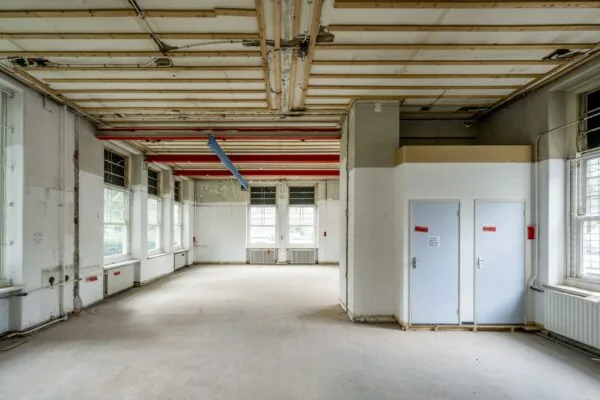 Leegstaand en deels gestripte ruimte in een oud gebouw aan het WG-plein met zichtbare leidingen en plafondconstructie.