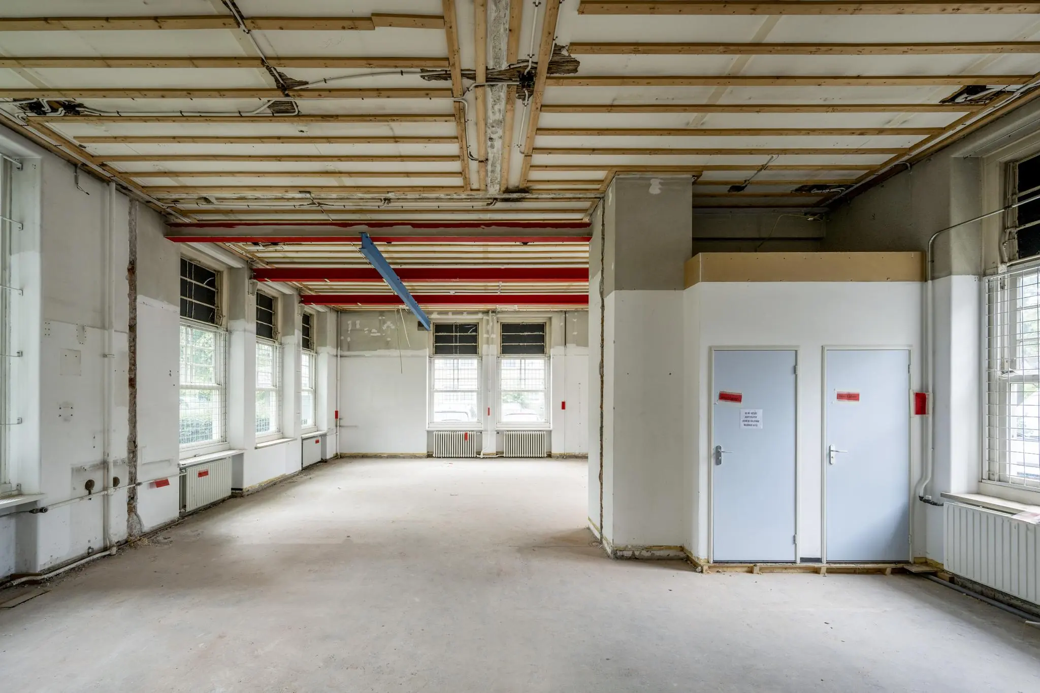 Leegstaand en deels gestripte ruimte in een oud gebouw aan het WG-plein met zichtbare leidingen en plafondconstructie.