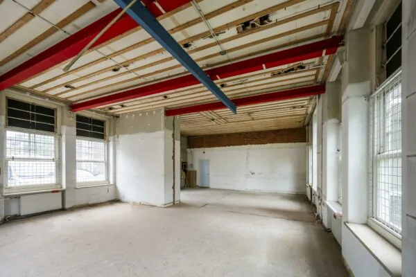 Leegstaand, industrieel ogend interieur met zichtbare rode en blauwe plafondbalken op het WG-plein.