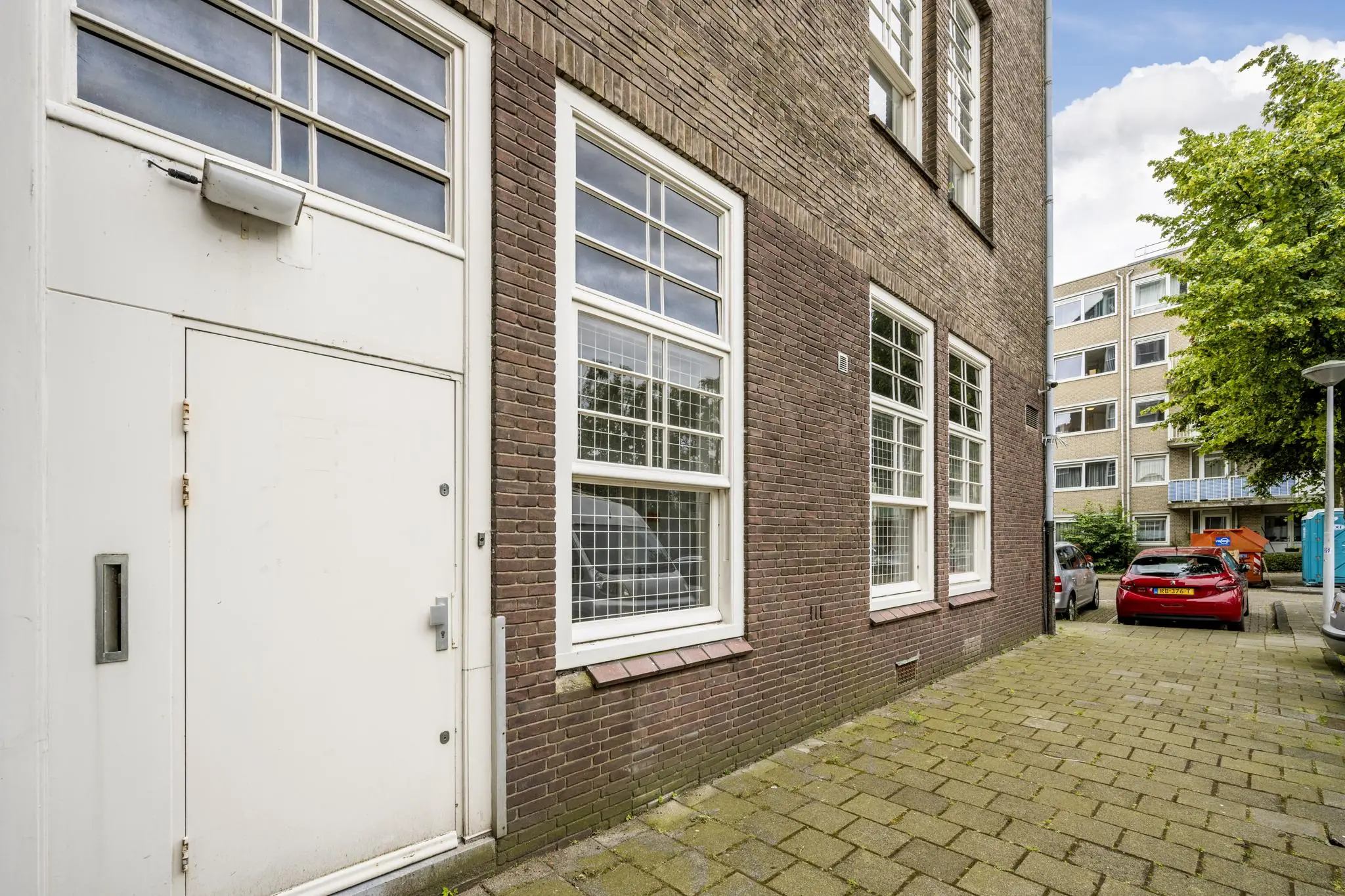 Ingang en gevel van een bakstenen gebouw aan het WG-plein met geparkeerde auto's op de achtergrond.