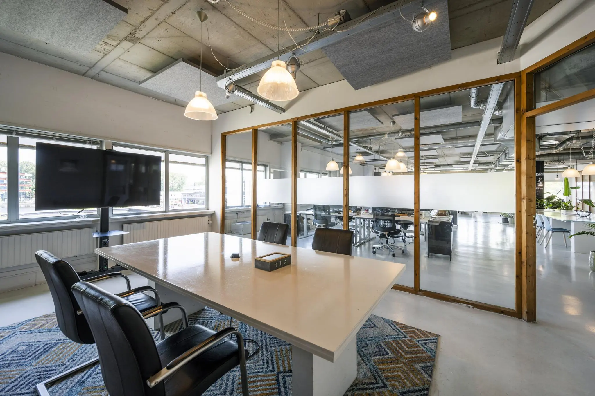 Vergaderruimte met een witte tafel, vier stoelen, een televisie en uitzicht op een modern kantoorpand aan de Anthony Fokkerweg.