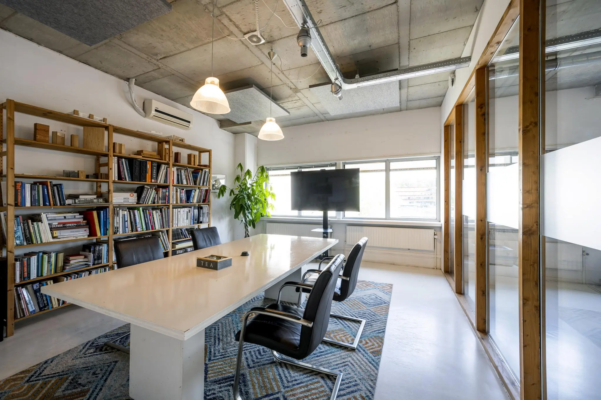 Vergaderruimte aan de Anthony Fokkerweg met een lange tafel, boekenrekken, stoelen en een flatscreen-tv.