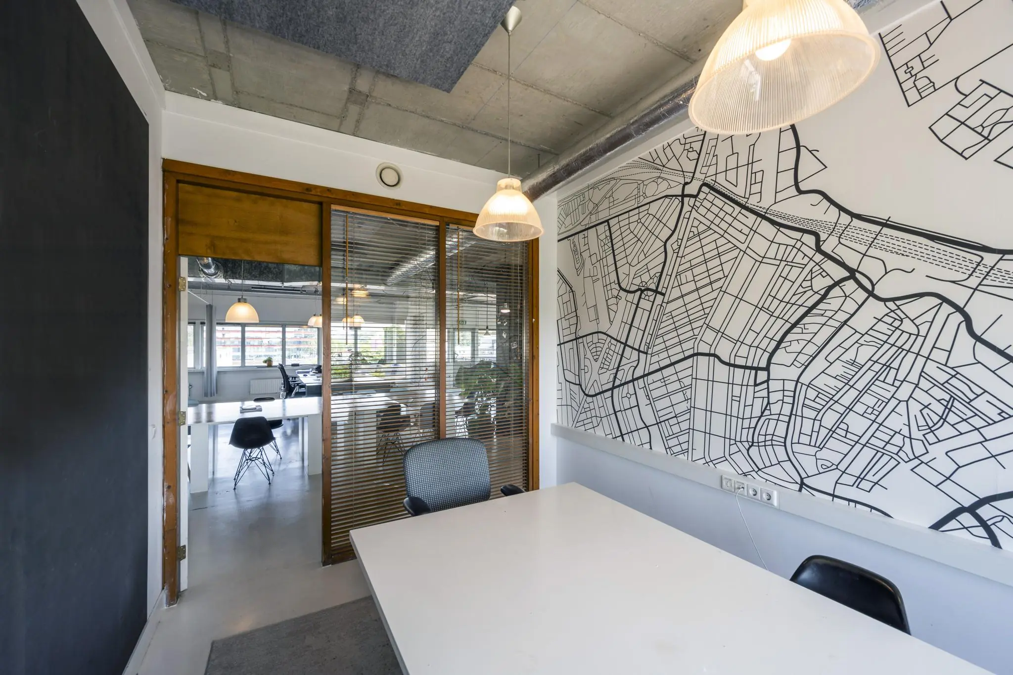 Vergaderruimte met witte tafel, designstoelen en een grote plattegrond van de omgeving van de Anthony Fokkerweg op de muur.