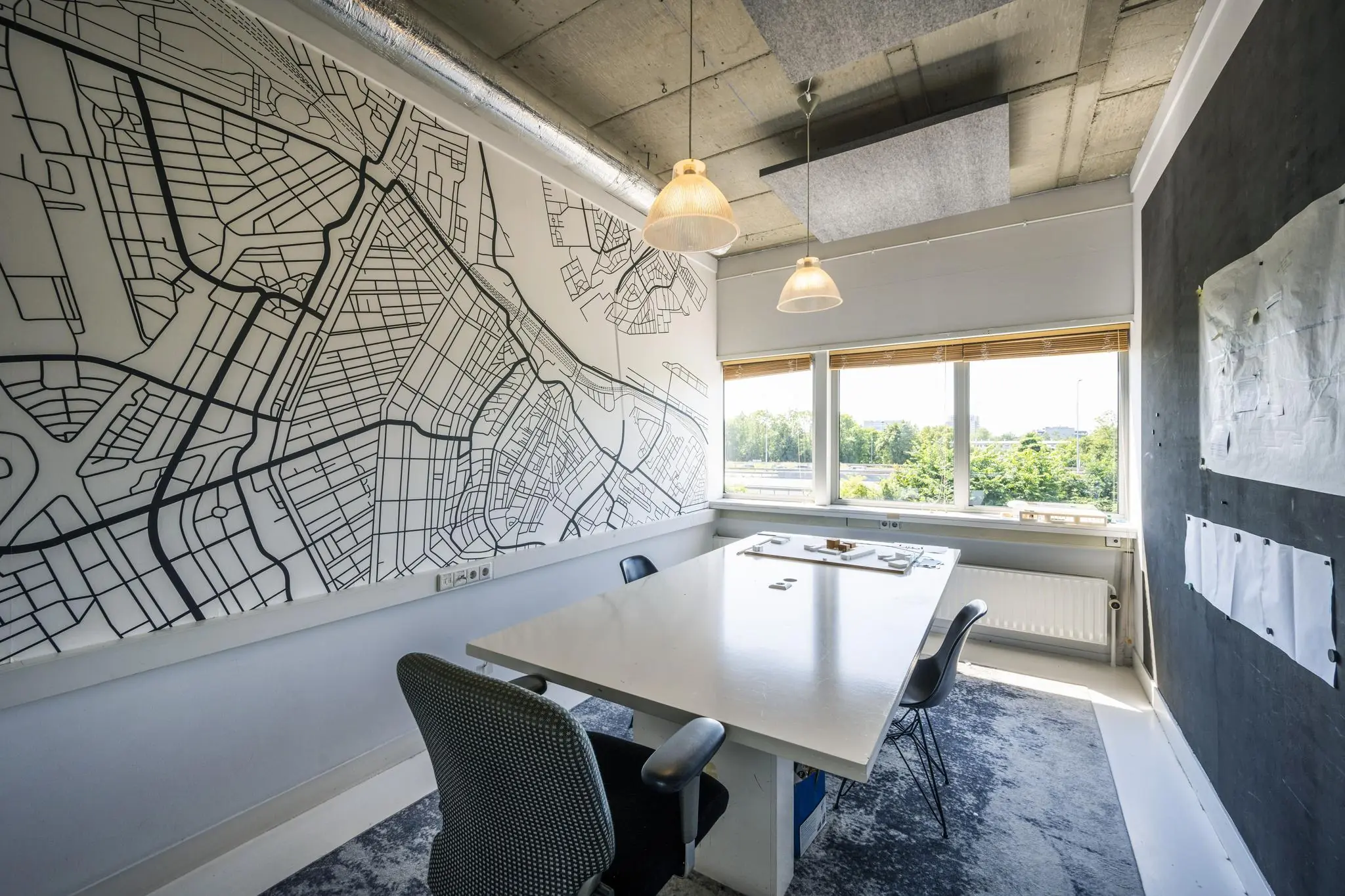 Vergaderruimte met een grote witte tafel, kaart van de omgeving rond Anthony Fokkerweg op de muur en uitzicht op groen buitengebied.