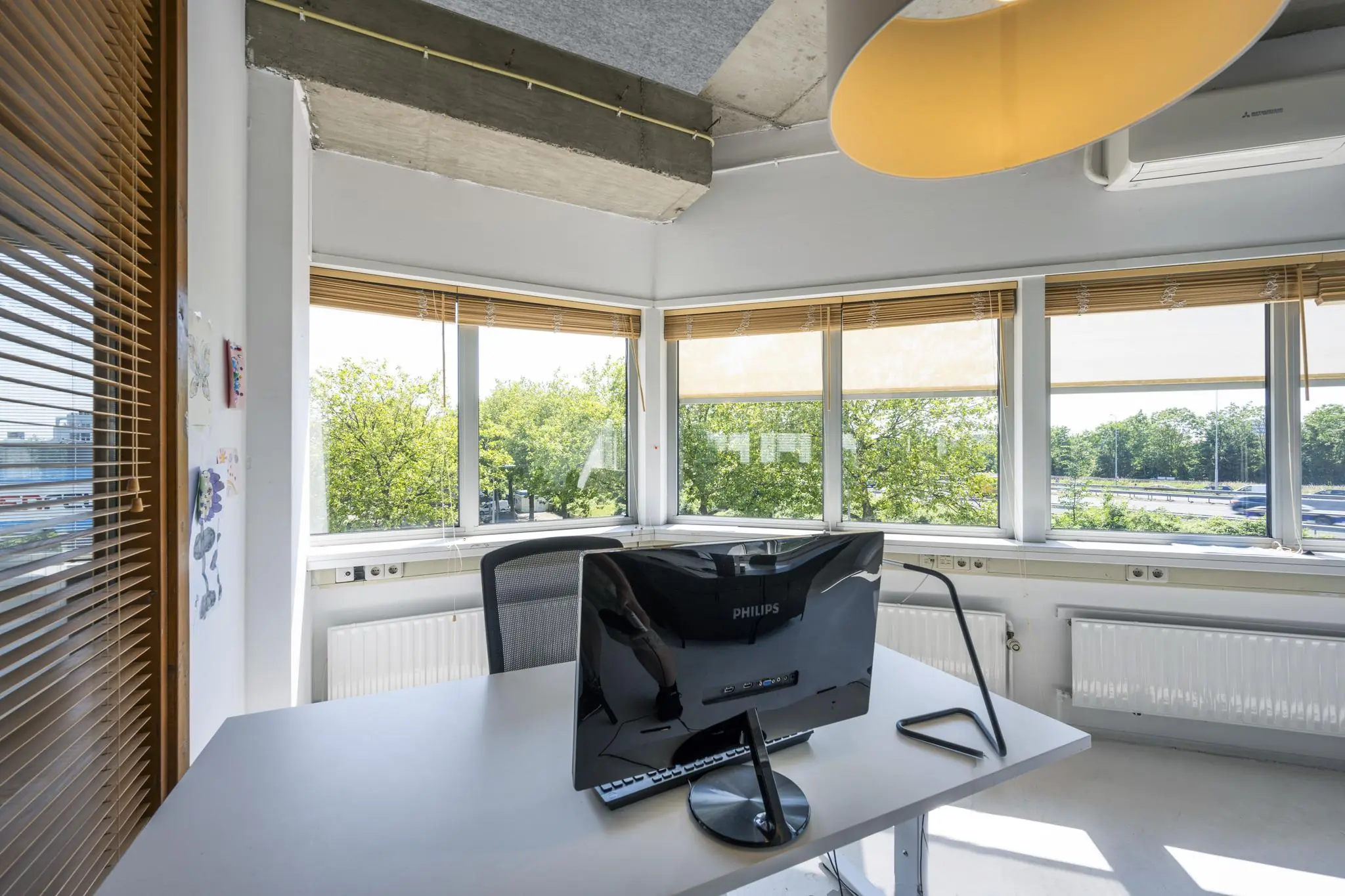 Licht en modern kantoor met een bureau en computerscherm, gelegen aan de Anthony Fokkerweg met uitzicht op groene bomen en een weg.