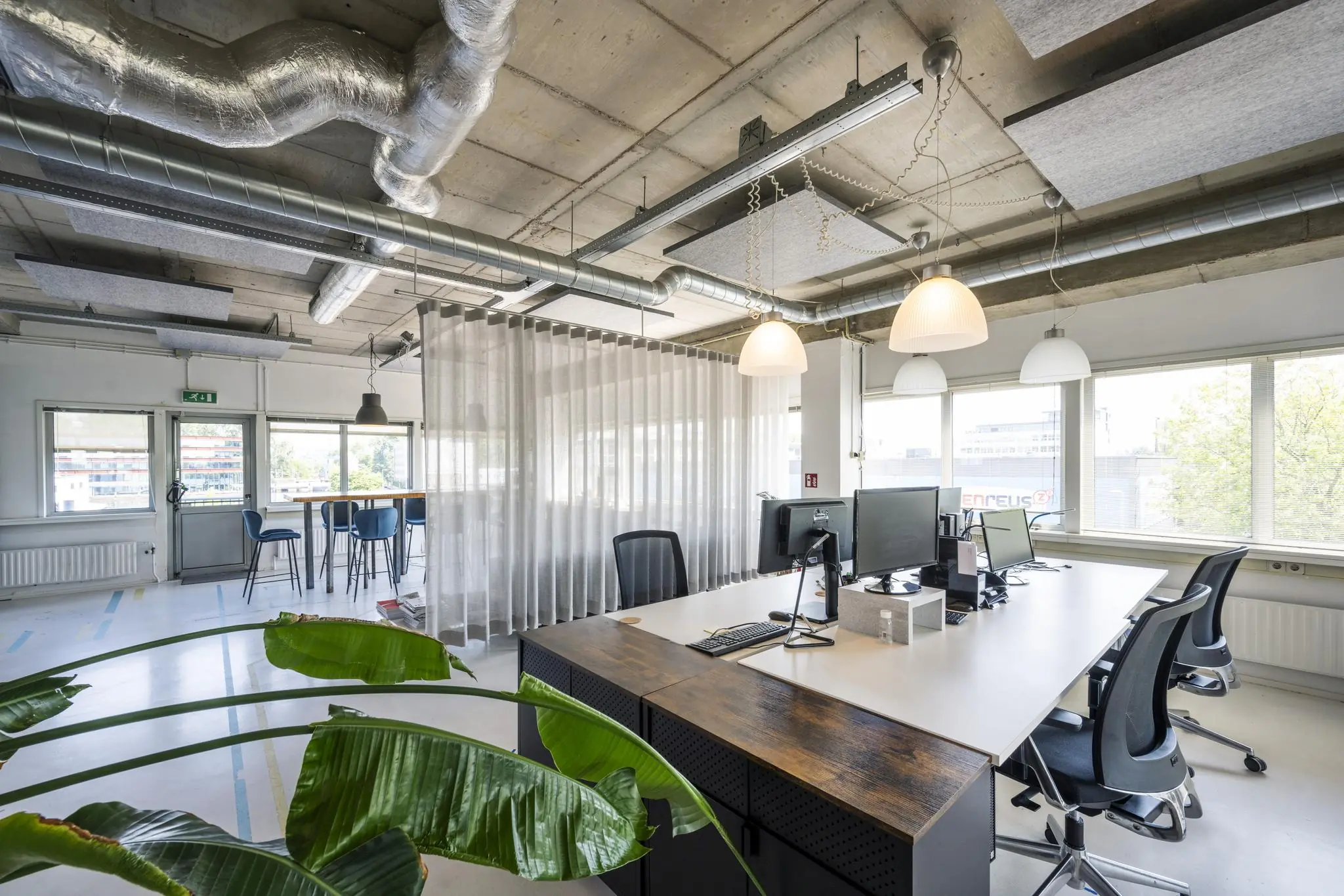 Modern kantoorinterieur aan de Anthony Fokkerweg met industriële plafonds, werkplekken en een zithoek bij het raam.
