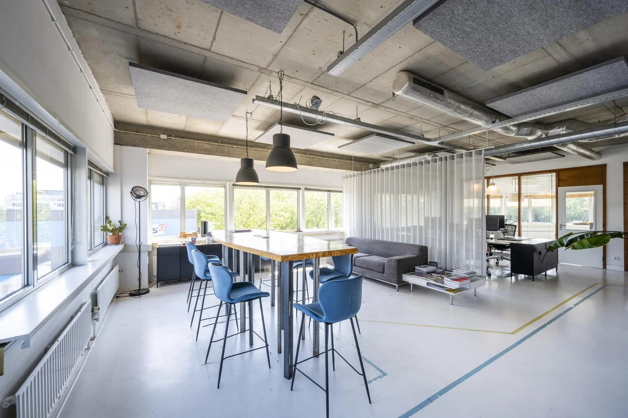 Modern ingerichte kantoorruimte aan de Anthony Fokkerweg met een hoge tafel, blauwe barkrukken, zithoek en veel natuurlijk licht.
