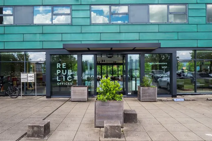 De ingang van het moderne kantoorgebouw "Republic Offices" met grote ramen en plantenbakken op de stoep.