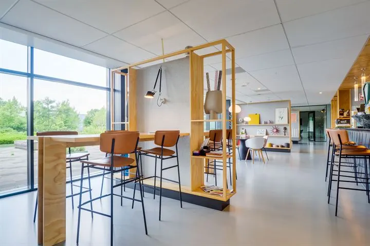 Moderne, open kantoorruimte met hoge zitplekken, veel daglicht en houten scheidingswanden.