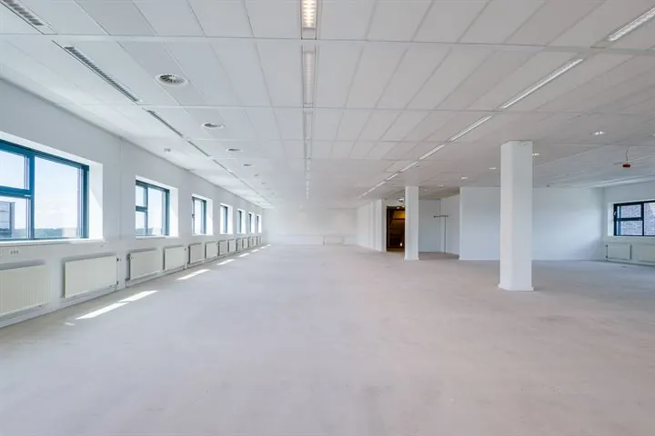 Leeg, wit kantoorpand met systeemplafond en grote ramen langs de linkerzijde aan de Ringwade.