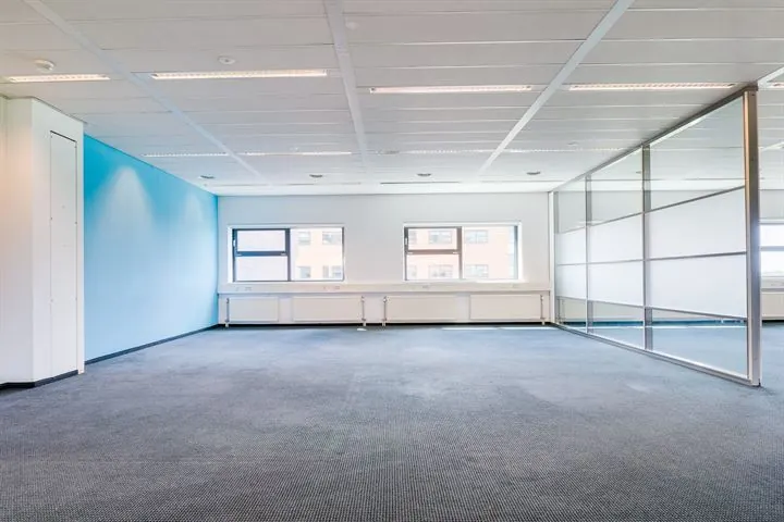 Leeg, modern kantoor met blauwe accentmuur en glazen scheidingswand aan de Ringwade.