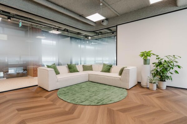 Moderne kantoorruimte aan de Joop Geesinkweg met een lichte hoekbank, groene accenten en kamerplanten op houten visgraatvloer.